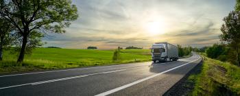 A truck driving down a highway next to a beautiful open field.