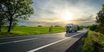 A truck driving down a highway next to a beautiful open field.