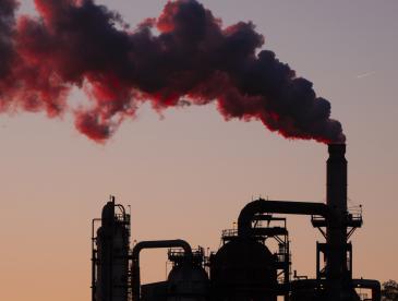 An industrial facility at sunset with billowing smoke coming out of it.