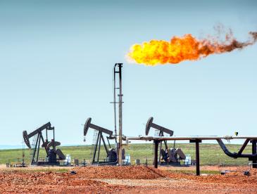 Flaring at a fossil fuel production facility sends flames into an open blue sky.