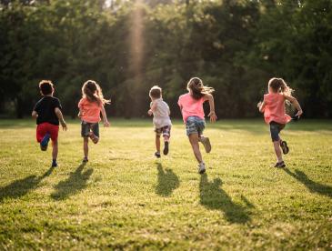 Back view children running together in public park at sunset