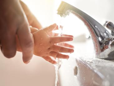 A baby's hands being washed in a bathroom sink