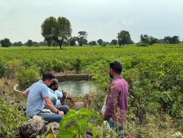 Three people grouped closely together by a water storage unit in a field. Photo: Ananya Revanna