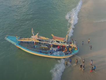 People walk along a beach to meet a fishing boat coming ashore.