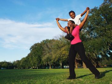 Smiling woman with a child on her shoulders in a beautiful park-like setting